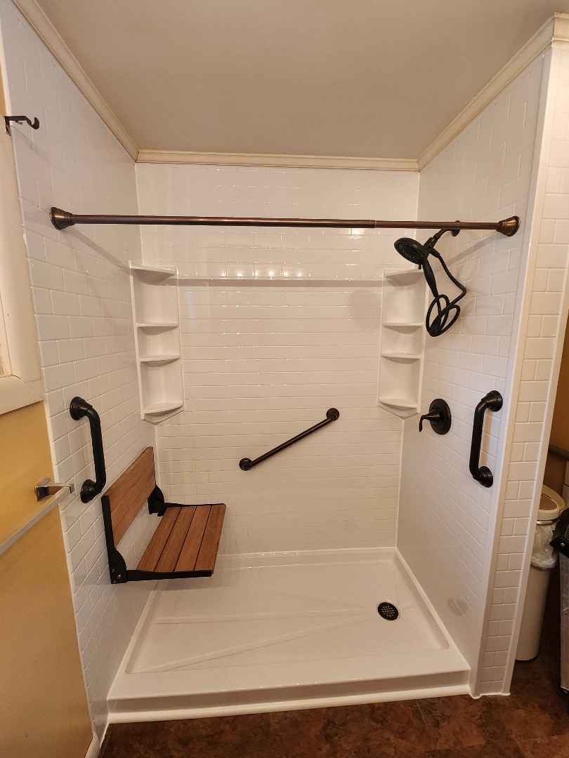Walk-in shower with a white base and a white subway tile acrylic wall-surround. Complete with oil-rubbed bronze fixtures and safety accessories.